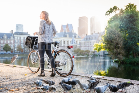 Vrouw loopt met fiets aan de hand langs de Haagse Hofvijver bij zonsopkomst