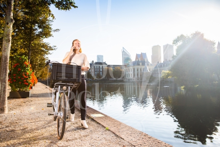 Vrouw loopt met fiets aan de hand langs de Haagse Hofvijver bij zonsopkomst