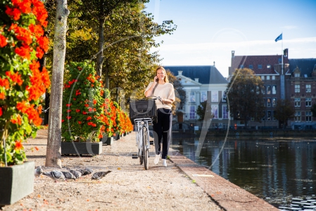 Vrouw loopt met fiets aan de hand langs de Haagse Hofvijver bij zonsopkomst