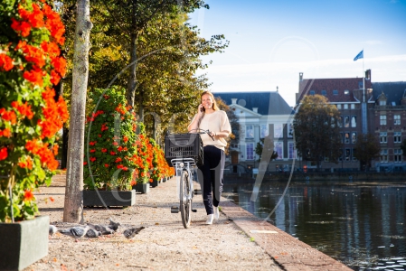 Vrouw loopt met fiets aan de hand langs de Haagse Hofvijver bij zonsopkomst