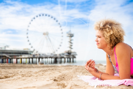 Meisje ligt op haar handdoek op Scheveningen met de Pier op de achtergrond