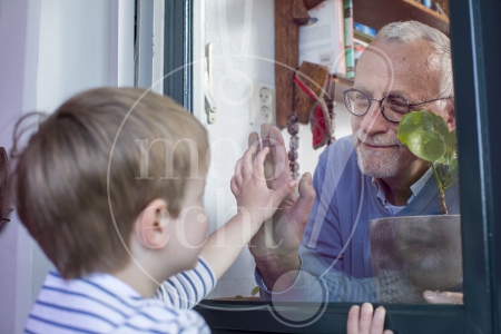 Jongetje en opa zien elkaar door raam tijdens Coronacrisis